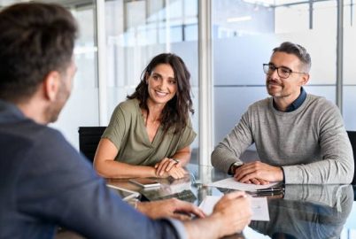 Smiling mature couple meeting with bank manager for investment. Beautiful mid adult woman with husband listening to businessman during meeting in conference room in modern office. Happy middle aged couple meeting loan advisor to buy a new home.